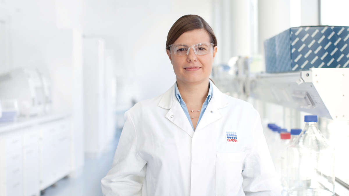 A woman in protective goggles and a lab coat standing in a lab